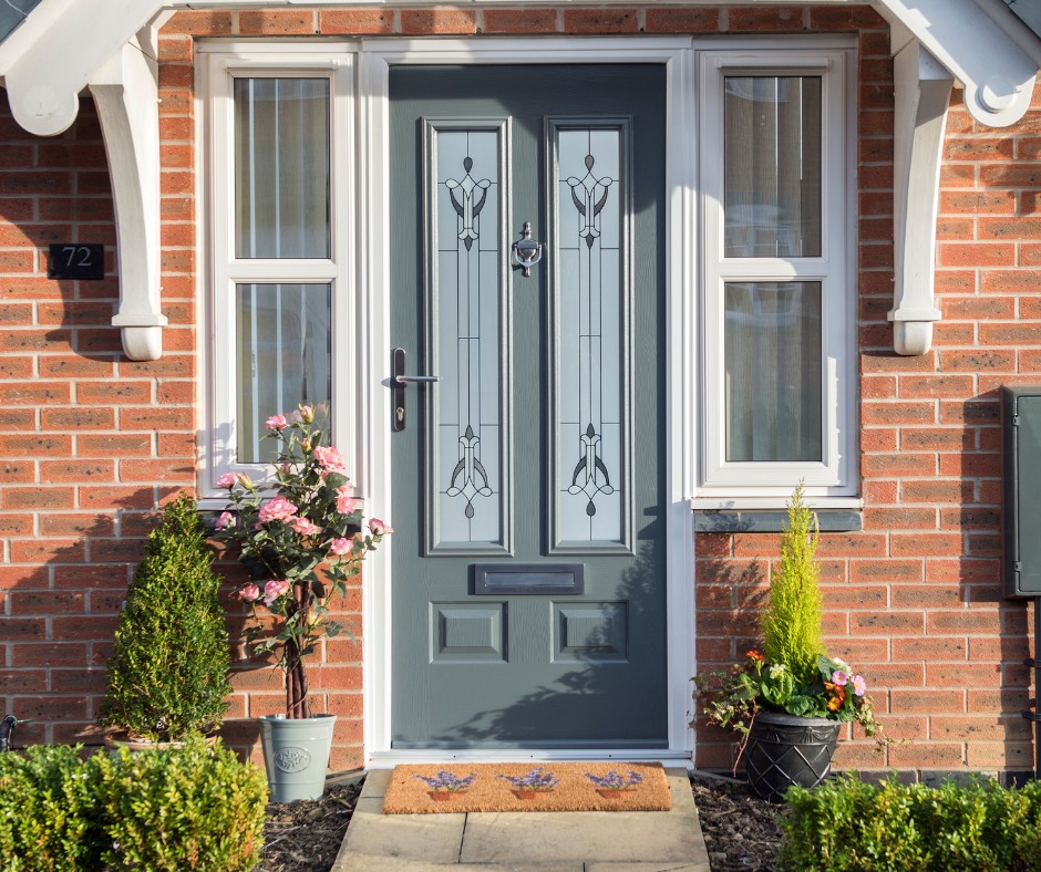 A grey front door with decorative glass panels from Cairnview Windows and Doors stands out on a red brick house. Potted plants and flowers flank the entrance, while stylish uPVC windows Perth add charm to the welcoming scene.
