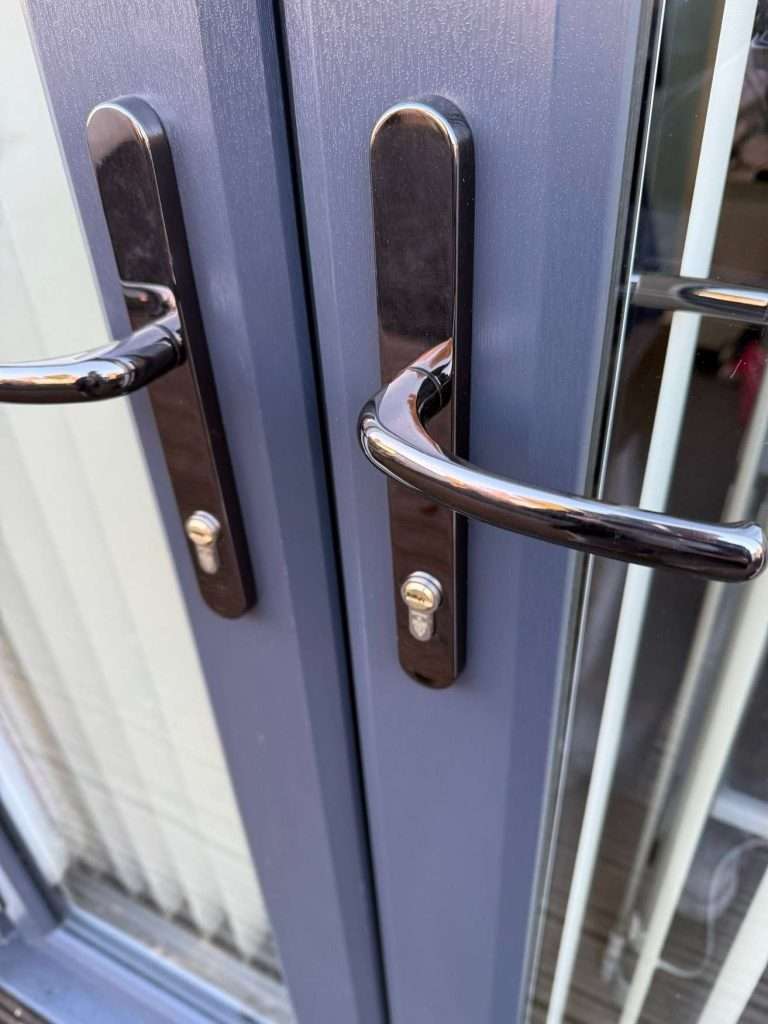 Close-up of two black door handles with keyholes on a dark blue double glass door, with vertical blinds visible through the glass on the right side.